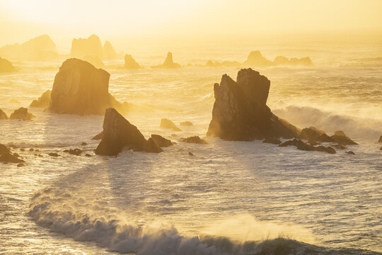 View of Silence Beach featuring jagged rock formations and crashing waves under the warm glow of a golden sunset Asturias, Asturias, Spain.