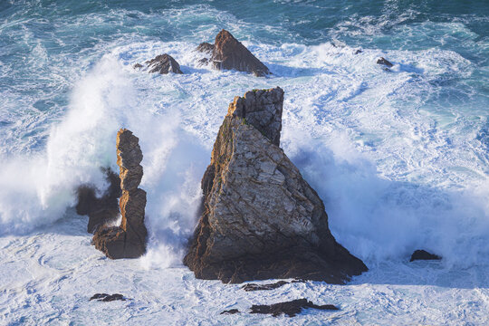 View of the jagged rock formations at Silence Beach with crashing white waves and turquoise ocean water in Asturias, Spain.