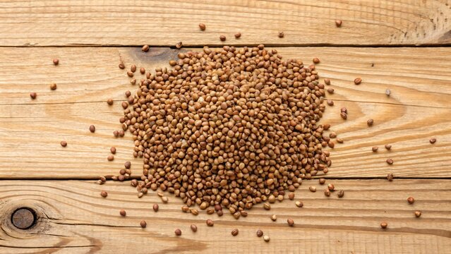 Pile of raw organic buckwheat groats scattered on a rustic wooden table surface, top-down view with natural lighting and organic texture.