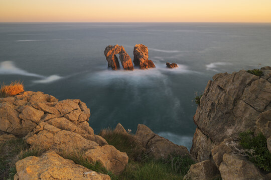 View of the Urros de Liencres rock formations and natural arch with long exposure water and golden sunset light from the cliffs Liencres, Cantabria, Spain.