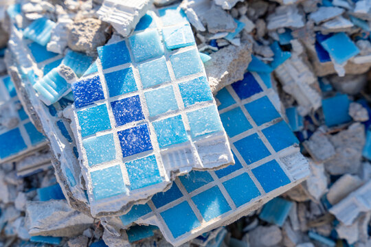 Broken blue and white ceramic mosaic tile fragment scattered on rough concrete rubble surface, urban destruction texture, renovation concept.