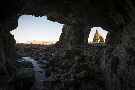 View of the rugged coastline and sea stacks through the opening of a dark sea cave at Playa de Campiechos Spain.