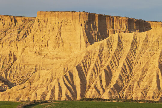 View of the dramatic eroded sandstone cliffs and plateaus of Bardenas Reales under warm golden light Navarre, Navarre, Spain.