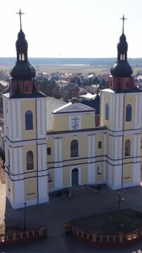 Vertical screen Drone Captures Church. Symmetrical Towers Framed Courtyard Scene. Bright Sky Illuminates Facade And Shadows Cast. Town Grid And Twin Towers Create Balanced Composition View