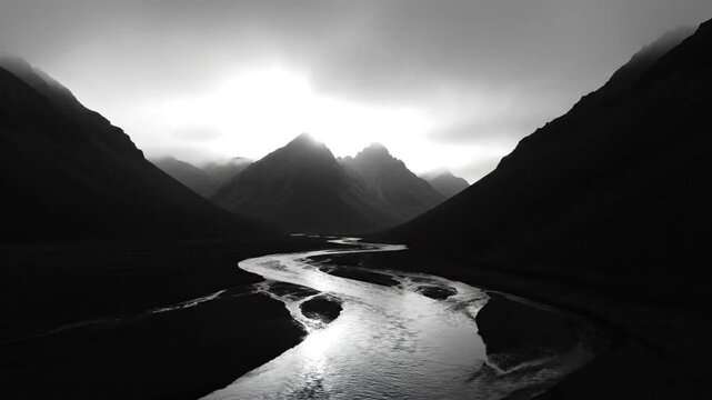 Serene black and white landscape of a winding river flowing between towering mountains under a cloudy sky.