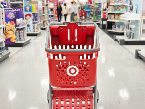 Walled Lake, Michigan, USA - May 2, 2026 : Close-up view of a red Target shopping cart in a bright retail store aisle with blurred shoppers and colorful merchandise in the background