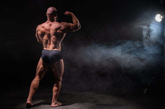 A male bodybuilder poses in shorts, showing off his back muscles.