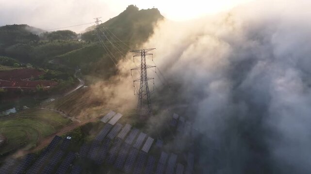 High voltage transmission tower and solar panels shrouded in mist on the mountain