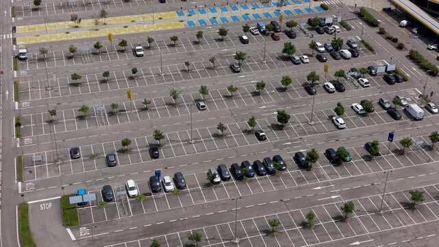 Aerial View of Parking Lot: An expansive outdoor parking lot, dotted with numerous cars parked in organized rows under a clear sky, with a few scattered trees providing sparse shade.