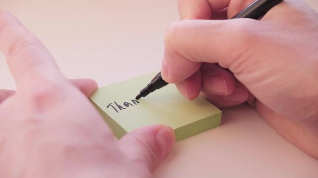 The process of writing the phrase Thank you on a yellow sticker with a black pen. Video footage of expressions of gratitude and courtesy.