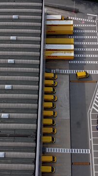 Logistics Hub Aerial View: An aerial perspective showcases a busy logistics hub with numerous yellow trucks lined up at loading docks, ready for distribution.
