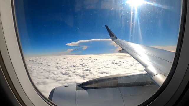 View from airplane window above clouds with sun shining.