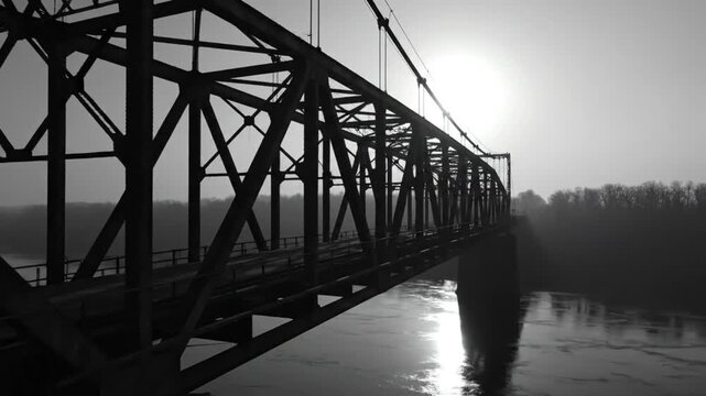 Black and white view of a steel truss bridge over a river on a hazy morning