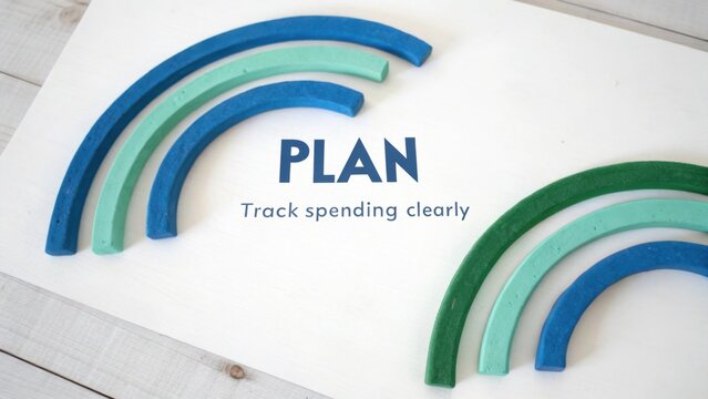 Colorful clay arches on a wooden surface with the word 'PLAN' and the phrase 'Track spending clearly' emphasizing financial organization and budgeting