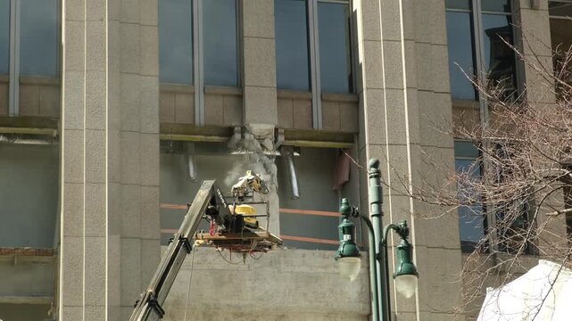 construction workers remove a section of a building in a city during the day