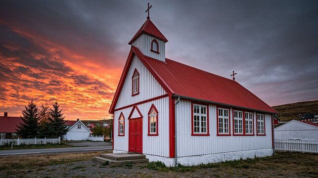 Traditional red accented white wooden christian church with red roof and crosses stands in small nordic village under vibrant orange dramatic sunset sky
