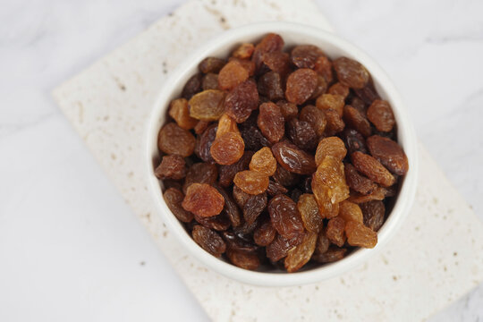 A bowl holds raisins on a plain surface