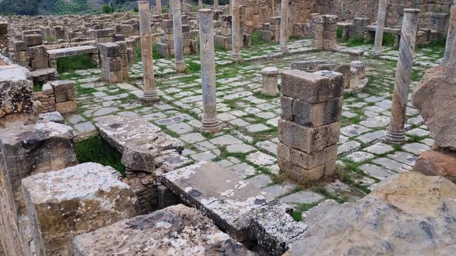 Public square within the ruins of Djemila, an ancient Roman archaeological city in Algeria, featuring columned remains and a central fountain in a historic marketplace setting