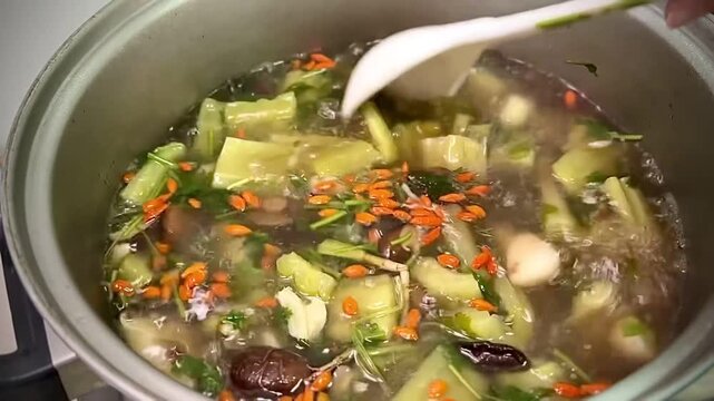 Stirring and serving a hot herbal bitter melon soup with a ladle