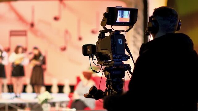 Professional cameraman filming live concert stage performance during television broadcast recording.