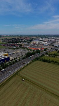 Urban sprawl encroaching on farmland, Aerial view of a highway passing through commercial buildings and agricultural fields under a clear blue sky.