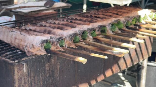 A long row of salt crusted whole fish on a smoking charcoal grill
