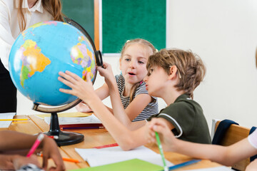 Students looking at a globe in a classroom, Children learning geography with a globe in classroom, Teacher and elementary students studying geography with a globe © JU.STOCKER