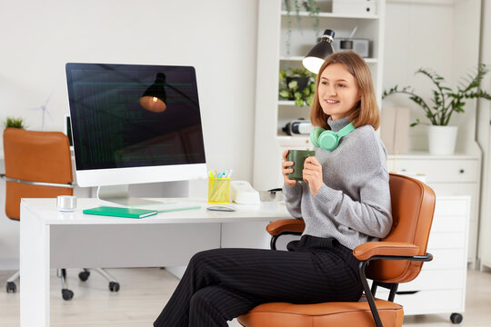 Happy female programmer with computer, cup of coffee and headphones working in office