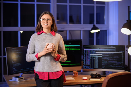 Female programmer with cup of coffee near workplace in office at night