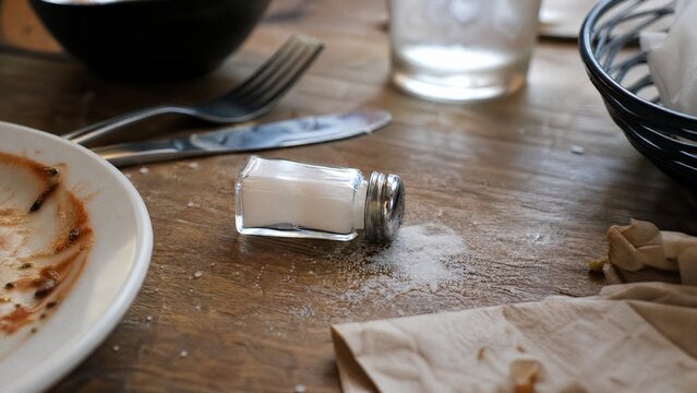 An overturned salt shaker on a dining table with scattered utensils in natural window light.