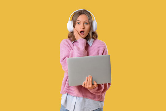 Shocked female programmer with laptop and headphones on yellow background