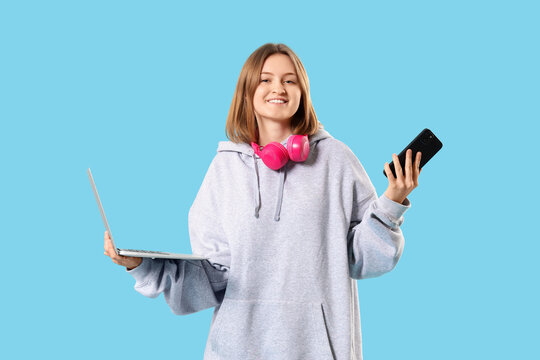 Happy female programmer with laptop, mobile phone and headphones on blue background