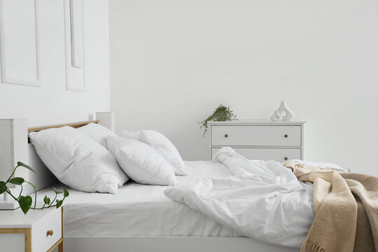 Interior of hotel room with commode, bedside table, unmade bed and crumpled linen near white wall