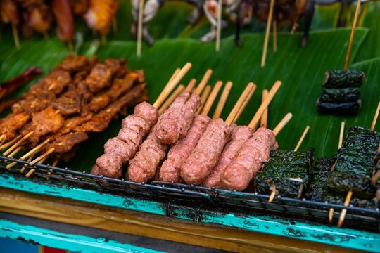 Traditional grilled pork meatballs nem nuong and meat wrapped in betel leaves bo la lot on skewers at outdoor street food market in Vietnam