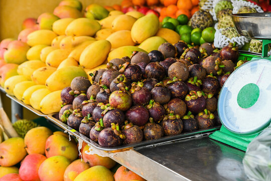 Fresh tropical fruits mangosteen and yellow mango on display at a local street market counter with scales in Vietnam organic agriculture product concept