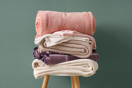 Stack of different cozy blankets on chair against turquoise background