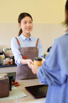 Asian female barista serving coffee takeaway cup smiling welcoming customer at cafe counter small business owner working service industry hospitality