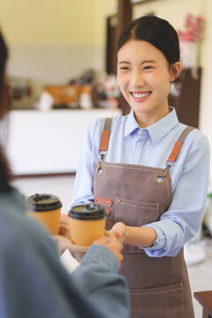 Asian barista woman serving coffee to customer at cafe counter wearing apron smiling friendly service hospitality small business owner working at coffee shop