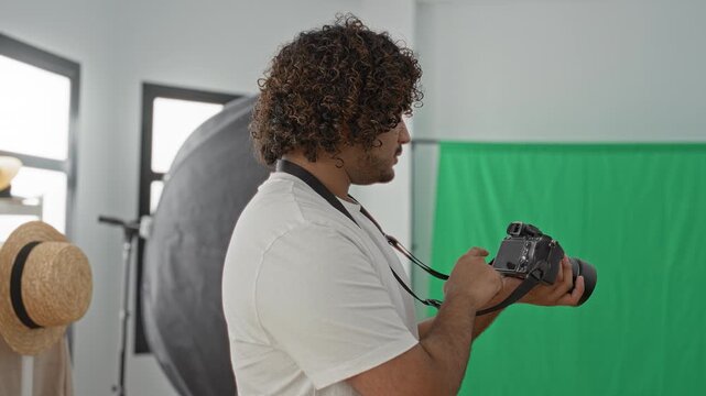 Young indian photographer holding dslr camera and adjusting settings in studio; concentration creativity.