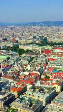Vertical video. Vienna, Austria. Aerial panoramic sweep over the UNESCO-listed historic center, dense terracotta rooftops and Baroque spires unfolding under clear summer sky. Drone footage. Rich colo