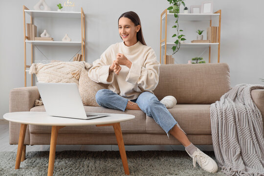 Young happy woman video chatting in sign language on sofa at home