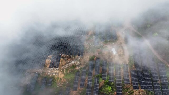 Aerial view of solar power station on misty hillside with rows of panels