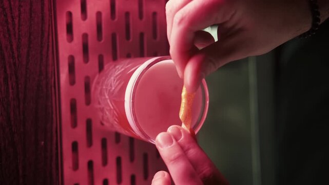Vertical video. Cosmopolitan cocktail. Pink beverage. Bartender hands serving garnished with lemon spiral zest in crystal glass.