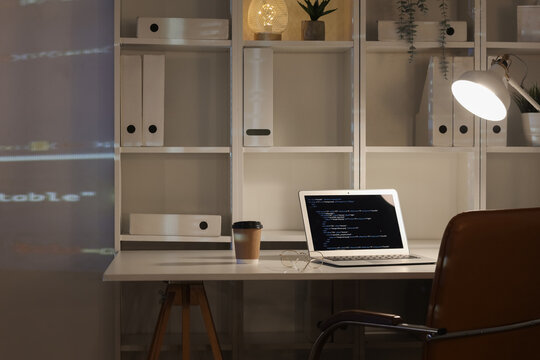 Laptop with programming code on table in dark office