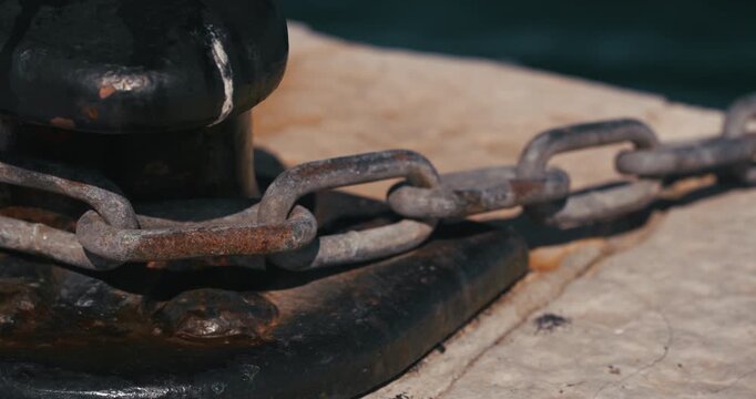 Close-up of a rusty metal chain attached to a mooring bollard on a marina pier.