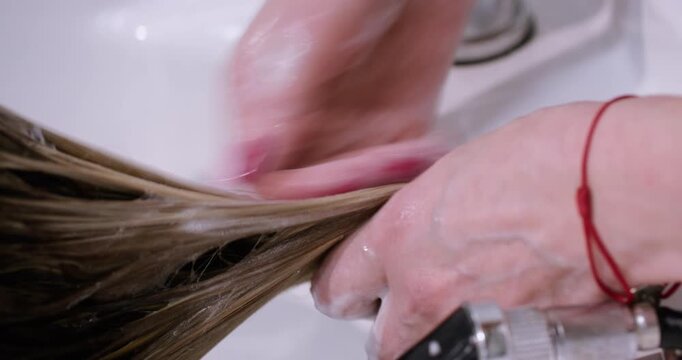 Hands washing hair. Salon routine. Female hairstylist working with client using water in sink for professional beauty treatment.