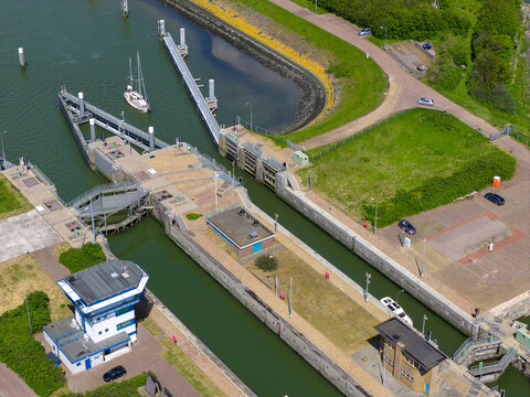 Aerial view of the Lorentzsluizen lock system with a sailboat navigating the canal next to green embankments and control buildings Kornwerderzand, Friesland, Netherlands.