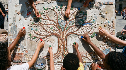 Fototapeta premium A group of people creating a mosaic art piece with a tree design on a sunny day outdoors