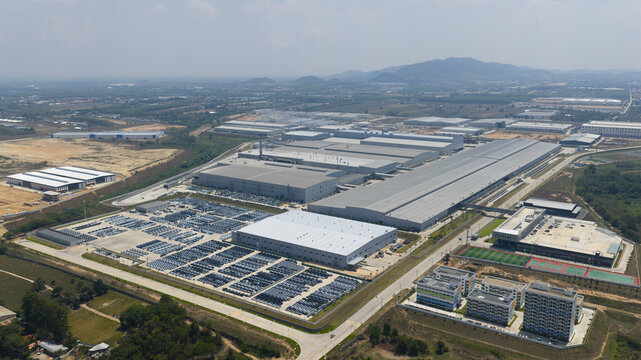 Aerial view of the BYD Thailand Rayong Office Building and vast industrial manufacturing complex with rows of parked vehicles and distant hills in Rayong, Thailand.