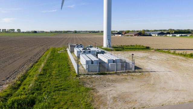 Aerial view of a large battery energy storage system in a fenced enclosure at the base of a wind turbine in a rural landscape Ooltgensplaat, South Holland, Netherlands.